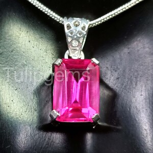 Peut inclure: Un collier pendentif argenté orné d'une pierre précieuse rectangulaire rose vif. La pierre est sertie dans un sertissage argenté et suspendue à une fine chaîne en argent. Le texte "Tulipgems" est visible sur le côté gauche du pendentif.