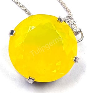 May include: A round, faceted, bright yellow gemstone pendant necklace. The gemstone is held in a silver setting and suspended from a silver chain. The text "Tulipgems" is printed on the gemstone.