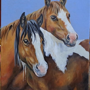 May include: An oil painting of two horses, one with a black mane and the other with a brown mane. Both horses have white markings on their faces and chests. The background is a light blue. The painting is signed by the artist, Ama Seguranyes.
