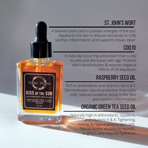 May include: A glass bottle of amber-colored liquid labeled "Kiss of the Sun Antioxidant Skin Elixir" with a dropper top. The bottle is sitting on a white surface with text about the ingredients and benefits of the product, including St. John's Wort, CoQ10, Raspberry Seed Oil, and Organic Green Tea Seed Oil.