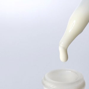 Op de afbeelding: Een witte druppelfles met een doorzichtige glazen fles en een witte plastic druppelaar. De druppelaar geeft een druppel witte vloeistof af.