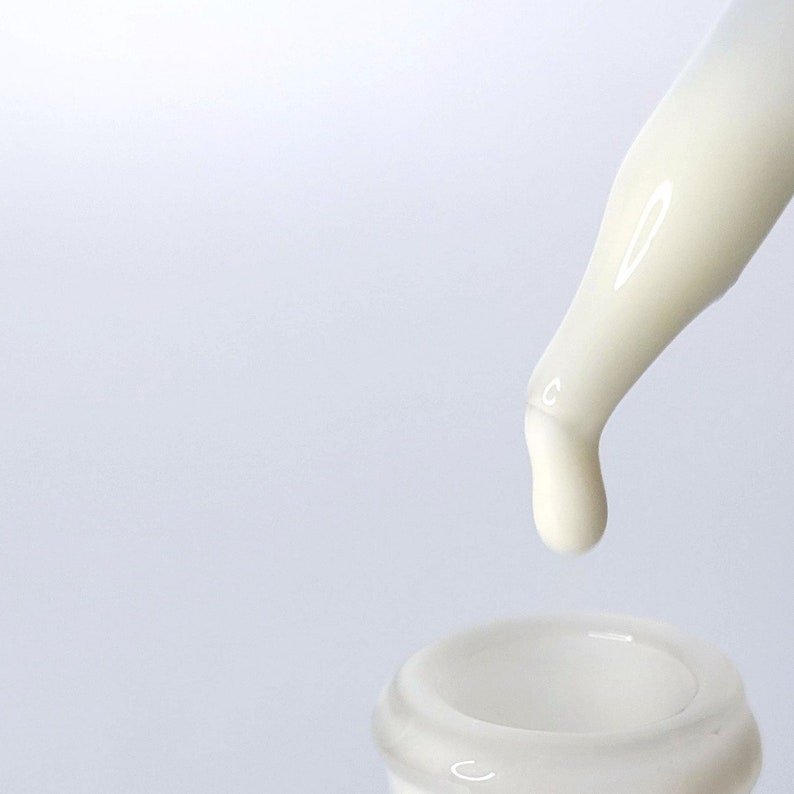 Op de afbeelding: Een witte druppelfles met een doorzichtige glazen fles en een witte plastic druppelaar. De druppelaar geeft een druppel witte vloeistof af.