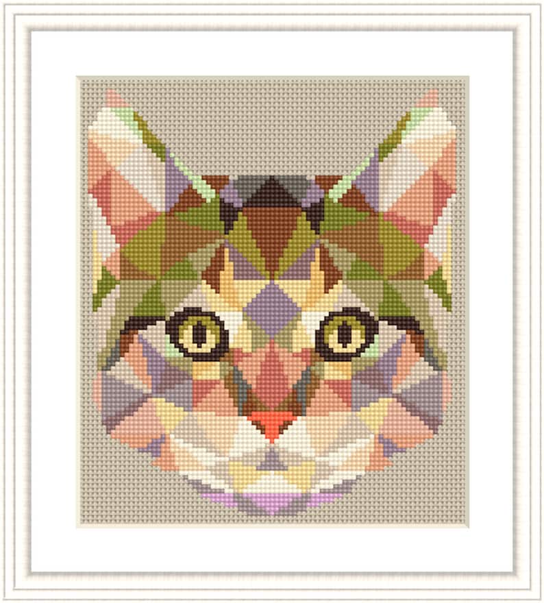 May include: A framed cross-stitch of a cat's face, featuring a geometric design. The cat's face is composed of various colored triangles, including shades of pink, green, brown, and purple. The eyes are yellow with black pupils, and the nose is red.