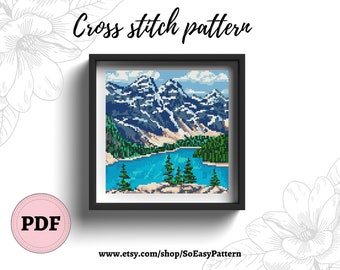 May include: Cross stitch pattern of a mountain lake scene with blue water, green trees, and snow-capped mountains. The pattern is framed in a black frame.