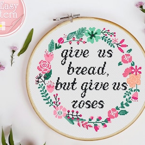 Puede incluir: Un aro de bordado blanco con un diseño de corona floral y el texto "give us bread, but give us roses".