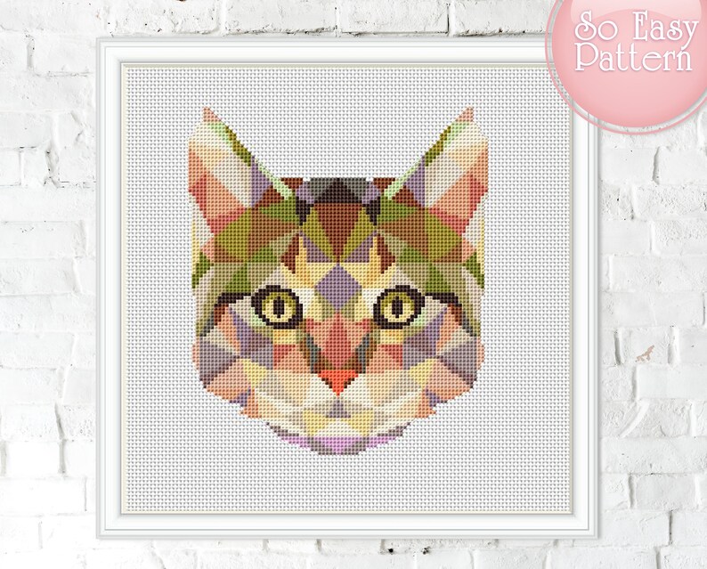 May include: A framed cross-stitch pattern of a cat's face, created with geometric shapes in shades of green, brown, yellow, and purple. The cat has large yellow eyes and a pink nose. The text "So Easy Pattern" is in the upper right corner.