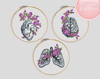 May include: Three embroidery hoop art pieces featuring anatomical illustrations of a heart, brain, and lungs. Each illustration is surrounded by purple flowers.