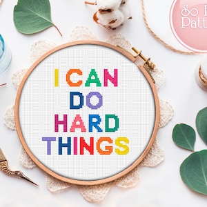 May include: A white embroidery hoop with the phrase "I CAN DO HARD THINGS" stitched in colorful thread. The letters are in a rainbow pattern.