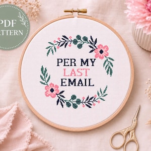 Puede incluir: Un bastidor de bordado circular de madera que contiene tela blanca con un diseño de punto de cruz. El diseño presenta una corona floral en tonos azul oscuro, verde y rosa, rodeando el texto en negro y rosa que dice PER MY LAST EMAIL.