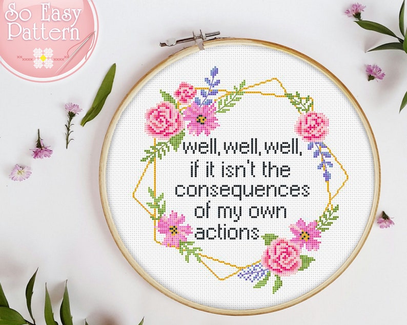 May include: A white embroidery hoop with a gold geometric frame and pink and purple flowers. The text inside the frame reads "well, well, well, if it isn't the consequences of my own actions."