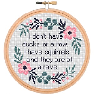 May include: A white embroidery hoop with a floral design around the edges. The hoop contains a cross-stitch design with the text "I don't have ducks or a row. I have squirrels and they are at a rave."