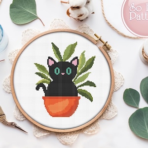 May include: A black cat with green eyes sits in a terracotta pot with green leaves. The cat is looking at the viewer. The pot is on a white background.