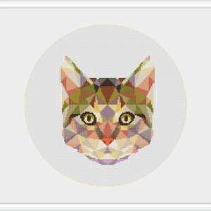 May include: A geometric cross-stitch design of a cat's face, featuring a mosaic of colorful triangles in shades of green, brown, pink, and purple. The cat's eyes are yellow, and the design is set against a white background within a white frame.