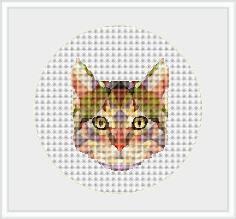 May include: A geometric cross-stitch design of a cat's face, featuring a mosaic of colorful triangles in shades of green, brown, pink, and purple. The cat's eyes are yellow, and the design is set against a white background within a white frame.