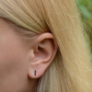 May include: A close-up of a person's ear with a small black bar stud earring. The earring is simple and minimalist.