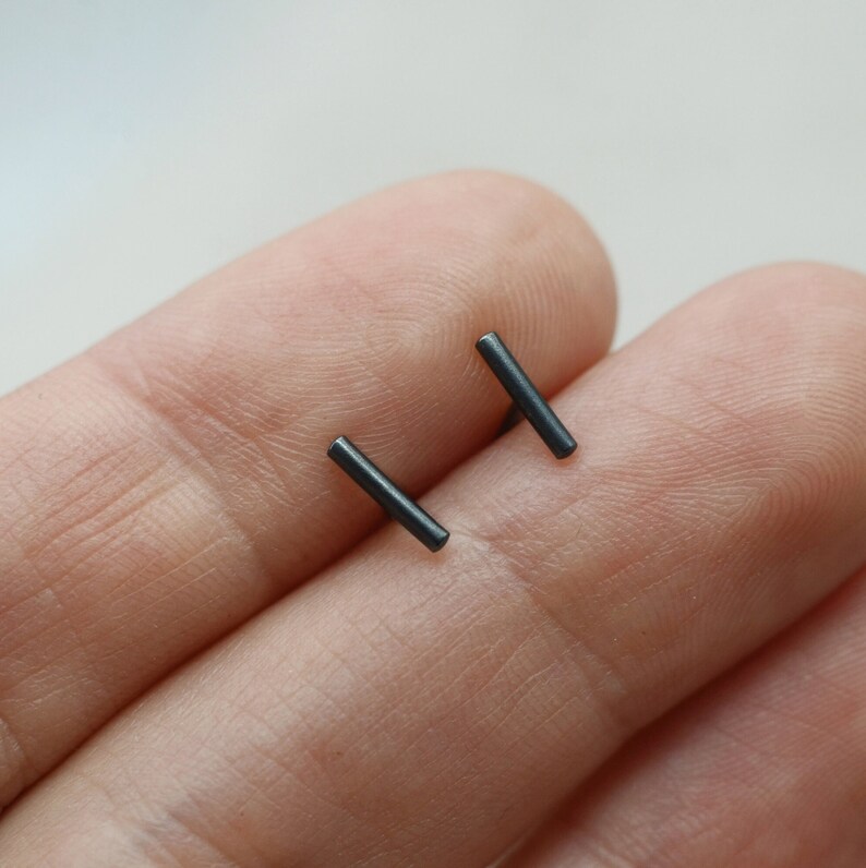 May include: A pair of black bar stud earrings. The earrings are small and simple, and they are made of a dark metal.