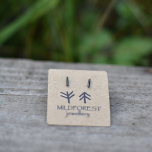 May include: A pair of black minimalist bar stud earrings on a brown card with the text "Mildforest Jewellery" and two stylised tree illustrations.