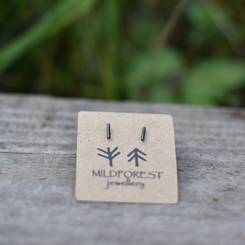 May include: A pair of black minimalist bar stud earrings on a brown card with the text "Mildforest Jewellery" and two stylised tree illustrations.