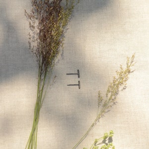 May include: A pair of minimalist black bar earrings on a light beige fabric background.