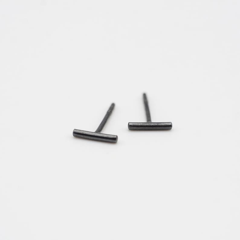 May include: A pair of minimalist black bar stud earrings. The earrings are made of a thin, black metal bar with a post and a back.