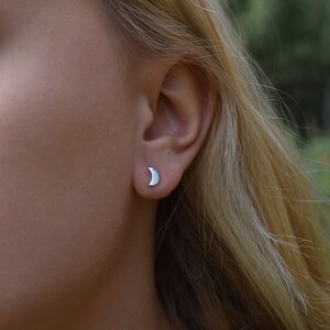 May include: A close-up of a person's ear with a small silver crescent moon stud earring.