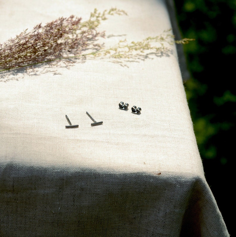 May include: A set of silver stud earrings with a bar design. The earrings are displayed on a white linen tablecloth.