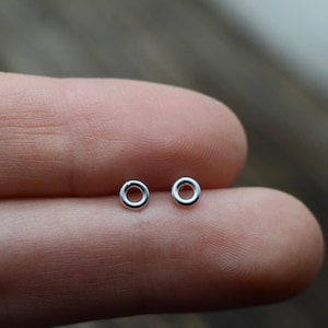 May include: A pair of small, silver hoop earrings. The hoops are simple and minimalist, with a smooth, polished finish.