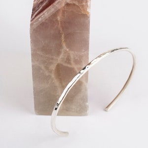Peut inclure: Un bracelet en argent martelé, posé sur un morceau de marbre vert et brun.