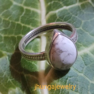 Puede incluir: Un anillo de plata con una piedra blanca en forma de lágrima engastada en el centro. El anillo está sobre una hoja verde.