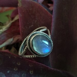 Op de afbeelding: Een zilveren ring met een blauwe maansteen ovale edelsteen gezet in een gedraaide band.
