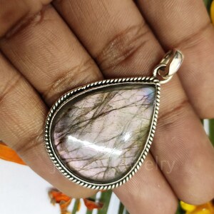 May include: A silver pendant with a teardrop-shaped labradorite gemstone. The stone has a iridescent sheen with shades of pink, gray, and blue.