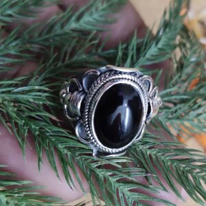 Può includere: Un anello d'argento con una pietra ovale nera incastonata in una fascia d'argento decorata.