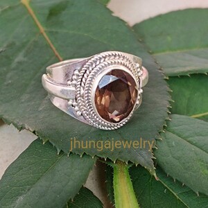May include: A silver ring with a brown gemstone set in a silver bezel. The ring has a detailed silver band with a braided design.