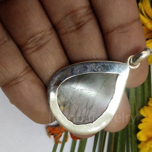 May include: A silver teardrop pendant with a gray gemstone. The pendant is set in a silver bezel and has a bail for attaching a chain.