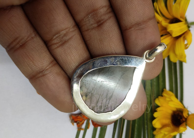 May include: A silver teardrop pendant with a gray gemstone. The pendant is set in a silver bezel and has a bail for attaching a chain.