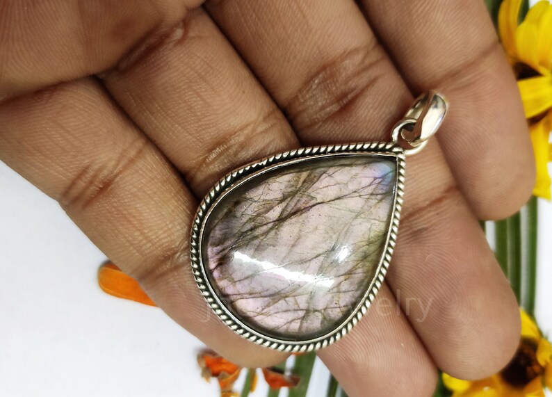 May include: A silver pendant with a teardrop-shaped labradorite gemstone. The stone has a iridescent sheen with shades of pink, gray, and blue.
