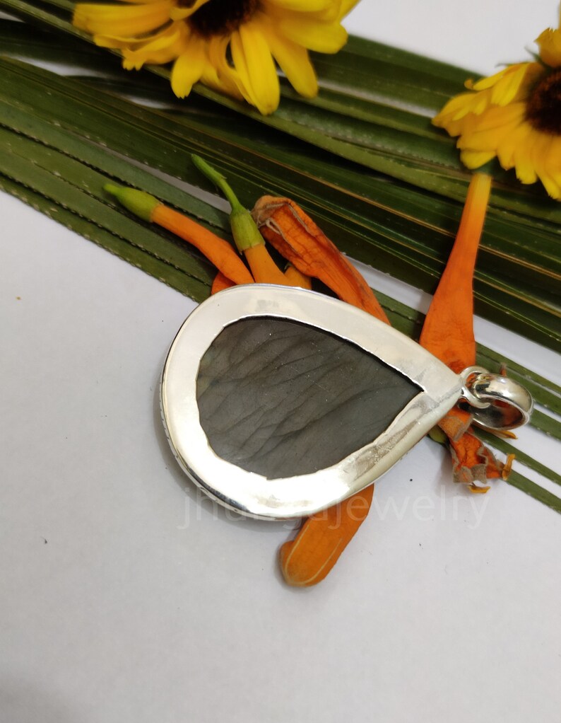 May include: A silver pendant with a teardrop-shaped labradorite gemstone. The pendant is set in a silver bezel and has a loop for attaching a chain.