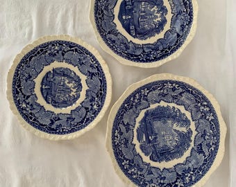 Puede incluir: Tres platos de cerámica azul y blanco con borde festoneado. Cada plato presenta un diseño floral azul y blanco con una imagen central de una casa.