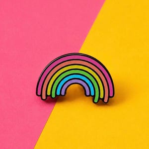 Könnte beinhalten: Eine Metall-Emaille-Anstecknadel in Form eines Regenbogens mit schwarzer Umrandung. Der Regenbogen besteht aus konzentrischen, gebogenen Streifen in Pink, Orange, Gelb, Grün, Blau und Lila. Die unteren Kanten wirken wie herabtropfende Farbe.