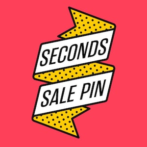 Può includere: Un nastro giallo e bianco con testo nero che recita "SECONDS SALE PIN". Il nastro è su uno sfondo rosa.