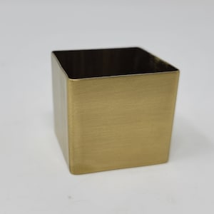 May include: A small, square, gold-colored metal container. The container has a brushed finish.