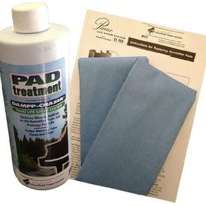 May include: A white bottle of piano pad treatment with the text "PAD treatment" and "DAMPP-CHASER PIANO LIFE SAVER SYSTEM" on the label. The bottle is next to a blue cloth and a sheet of paper with instructions for replacing humidifier pads.