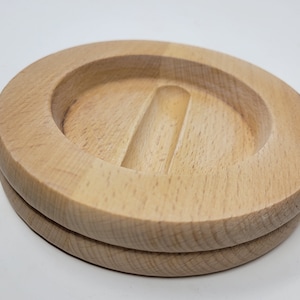 May include: Two round wooden coasters with a groove in the centre. The coasters are made of light wood and are stacked on top of each other.