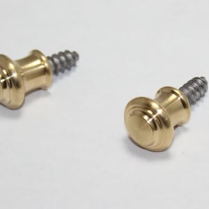 May include: Two brass-colored cabinet knobs with a screw base. The knobs have a rounded, tiered design and a shiny finish. The screws are silver-colored and have a spiral pattern.