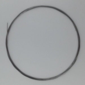 May include: A thin, dark grey wire is coiled into a circle, centred against a plain, light grey background. The wire appears to be made of metal and is slightly reflective. The overall image is simple and minimalist.