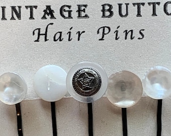 Könnte beinhalten: Ein Set aus fünf Vintage-Haarnadeln auf einer weißen Karte. Die Nadeln haben schwarze Stiele und knopfförmige Köpfe in Weiß und Klar. Eine Nadel hat einen Knopf mit Sternmuster. Auf der Karte steht "VINTAGE BUTTON Hair Pins".