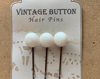 Könnte beinhalten: Drei Haarnadeln mit weißen Kugelspitzen auf einer dekorativen Karte. Auf der Karte steht "VINTAGE BUTTON Hair Pins" in einer Vintage-Schriftart. Die Karte hat ein dekoratives, spitzenartiges Muster. Die Nummer "14" ist handschriftlich unten rechts.
