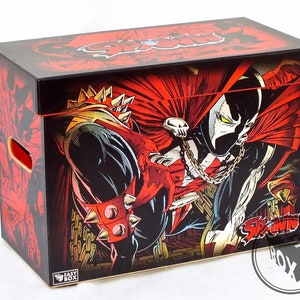 Puede incluir: Una caja de almacenamiento de cómics negra y roja con el personaje Spawn. La caja tiene tapa y asas, con el logotipo y la obra de arte de Spawn en un lugar destacado. La caja es de cartón.