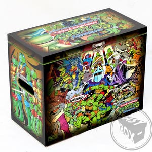 Op de afbeelding: Een rechthoekige opbergdoos met een scharnierend deksel, versierd met een levendige stripachtige illustratie van Teenage Mutant Ninja Turtles-personages. De doos heeft een metalen sluiting. De zijkanten en bovenkant zijn bedekt met kleurrijk artwork, met de woorden "Teenage Mutant Ninja Turtles Adventures" zichtbaar.
