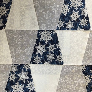 Puede incluir: Primer plano de una colcha de tela con un patrón repetitivo de copos de nieve en tonos azules, blancos y grises.